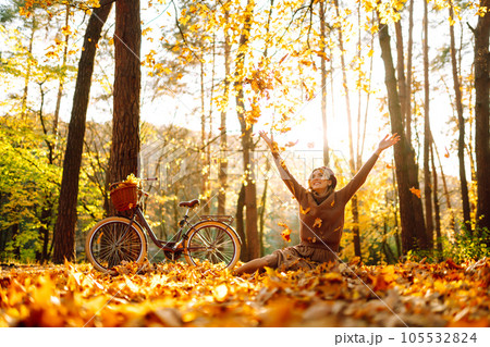 Stylish woman with a bicycle enjoying autumn weather in the park. Beautiful Woman in the autumn forest. 105532824