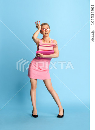 Hard work. Full lenght photo of busy girl dressed business in pink colors, with heavy stack of books and looking away on blue studio background. 105532901