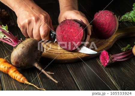 The cook cuts beetroot with a knife to prepare delicious borscht. Ukrainian national cuisine The cook cuts beetroot with a knife to prepare delicious borscht. Ukrainian national cuisine 105533924