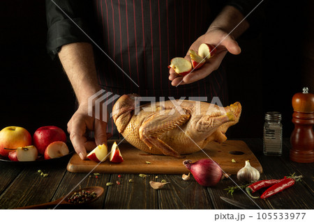 Adding apples to raw duck before cooking by the cook's hands. Raw duck on the kitchen table and cutting board. Working environment in a restaurant kitchen Adding apples to raw duck before cooking by the cook's hands. Raw duck on the kitchen table and cutting board. Working environment in a restaurant kitchen 105533977
