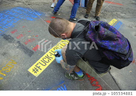 Young man activist painting offensive lettering against Putin on asphalt with a can spray. Kyiv, Ukraine Young man activist painting offensive lettering against Putin on asphalt with a can spray. Kyiv, Ukraine 105534881