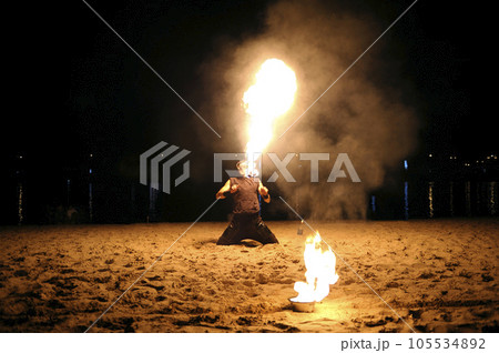 Man fire juggler performing at night on a sandy beach 105534892