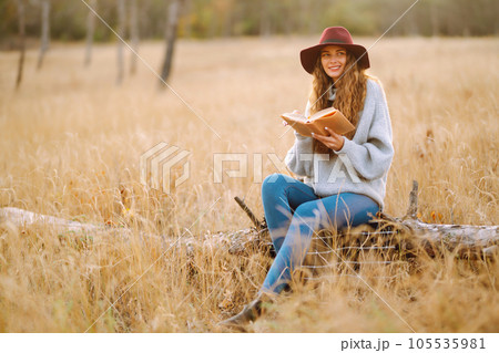 Fall picnic in nature. Young woman sitting on the blanket reading a book and smiling outdoors. 105535981