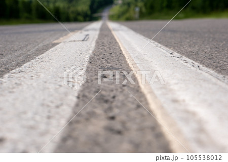 Country road with markings in the middle of the forest. Path and forward movement in the sun. Beautiful, green forest in the spring at sunset. Concept for success in the future goal and passing time Country road with markings in the middle of the forest. Path and forward movement in the sun. Beautiful, green forest in the spring at sunset. Concept for success in the future goal and passing time 105538012