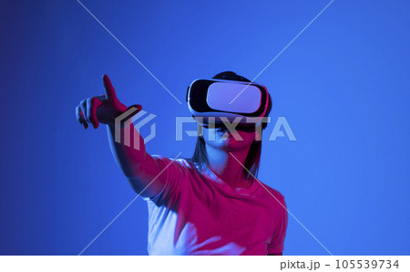 Brunette woman in VR headset looking up at the objects in virtual reality. VR is a computer technology that simulates a physical presence and allows the user to interact with environment. Brunette woman in VR headset looking up at the objects in virtual reality. VR is a computer technology that simulates a physical presence and allows the user to interact with environment. 105539734