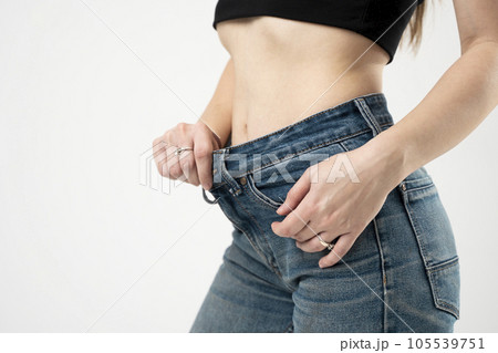 Slim woman showing slim body after sport trainings, healthy eating. Weight loss concept. Dieting. Thin woman in big blue jeans pants, weight loss concepts. Slim girl wearing oversized pants. Slim woman showing slim body after sport trainings, healthy eating. Weight loss concept. Dieting. Thin woman in big blue jeans pants, weight loss concepts. Slim girl wearing oversized pants. 105539751