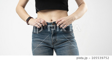 Cropped view of young woman in big blue jeans demonstrating results of her slimming program. Healthy eating at home. Successful weight loss diet concept. 105539752