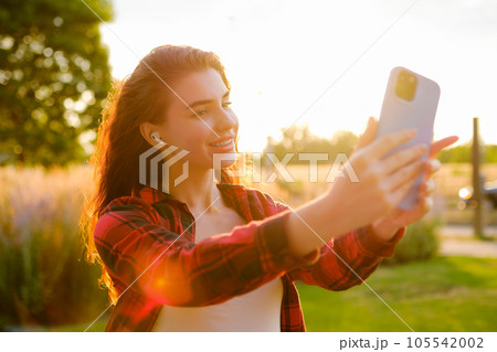 Beautiful curly red hair taking selfie using a smartphone standing in the street Beautiful curly red hair taking selfie using a smartphone standing in the street 105542002
