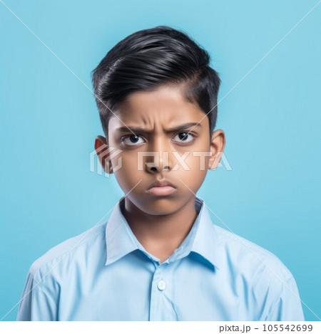 Portrait of a serious Indian teenage boy with short black hair. Closeup face of an unhappy Indonesian teenager on a blue background looking at camera. Front view of an unsmiling kid in a blue shirt. 105542699