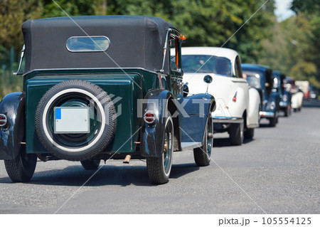 Row of old vintage cars driving down the road on sunny day, view form behind 105554125