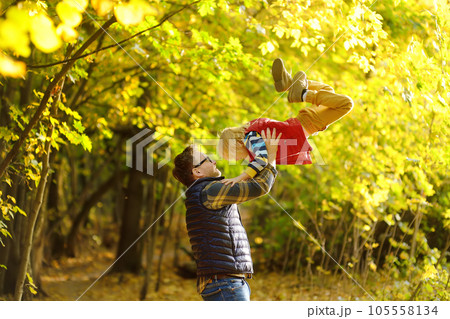 Little boy and his father having fun during stroll in the forest on sunny autumn day. Dad throws child up. Quality family time outdoor. 105558134