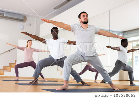 Man practising warrior two pose with group in gym Man practising warrior two pose with group in gym 105558665