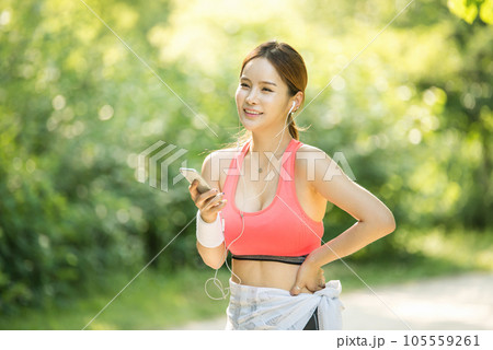A beautiful woman wearing sportswear and exercising while listening to music on her smartphone in the park A beautiful woman wearing sportswear and exercising while listening to music on her smartphone in the park 105559261