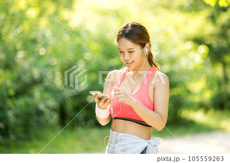 A beautiful woman wearing sportswear and exercising while listening to music on her smartphone in the park A beautiful woman wearing sportswear and exercising while listening to music on her smartphone in the park 105559263
