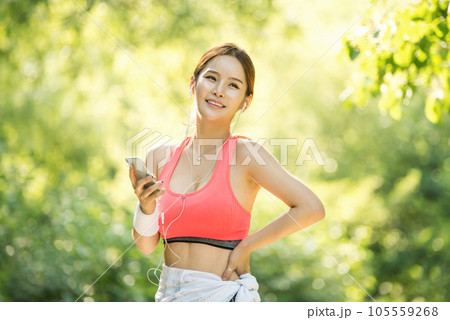 A beautiful woman wearing sportswear and exercising while listening to music on her smartphone in the park A beautiful woman wearing sportswear and exercising while listening to music on her smartphone in the park 105559268