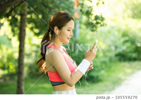 A beautiful woman wearing sportswear and exercising while listening to music on her smartphone in the park A beautiful woman wearing sportswear and exercising while listening to music on her smartphone in the park 105559270