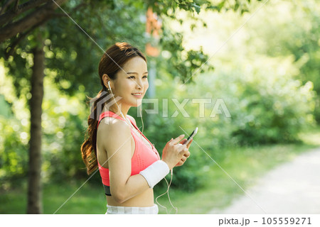 A beautiful woman wearing sportswear and exercising while listening to music on her smartphone in the park A beautiful woman wearing sportswear and exercising while listening to music on her smartphone in the park 105559271