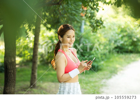A beautiful woman wearing sportswear and exercising while listening to music on her smartphone in the park A beautiful woman wearing sportswear and exercising while listening to music on her smartphone in the park 105559273