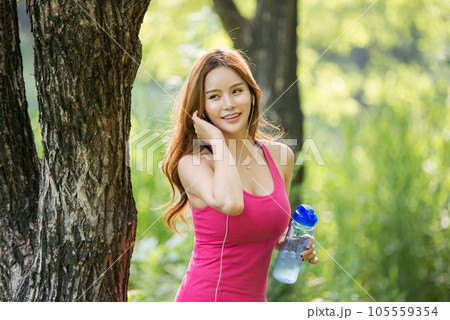 A beautiful woman holding a water bottle in the park while listening to music during morning exercise A beautiful woman holding a water bottle in the park while listening to music during morning exercise 105559354