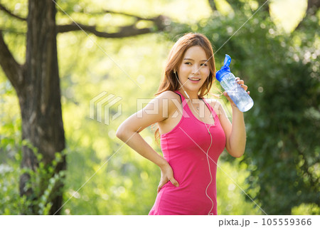 A beautiful woman holding a water bottle in the park while listening to music during morning exercise 105559366