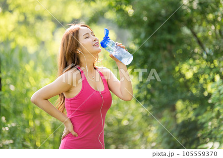 A beautiful woman holding a water bottle in the park while listening to music during morning exercise A beautiful woman holding a water bottle in the park while listening to music during morning exercise 105559370