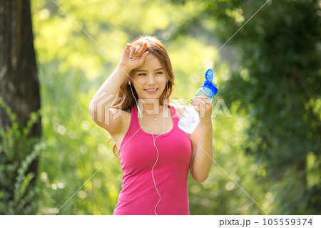 A beautiful woman holding a water bottle in the park while listening to music during morning exercise 105559374