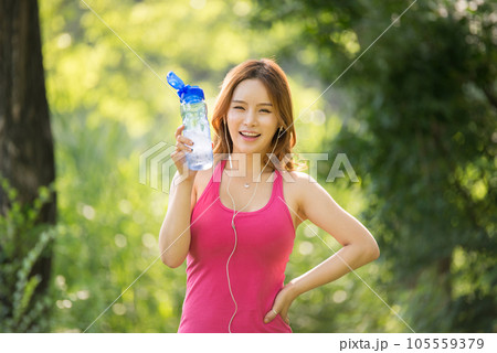 A beautiful woman holding a water bottle in the park while listening to music during morning exercise 105559379