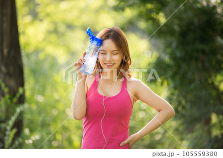 A beautiful woman holding a water bottle in the park while listening to music during morning exercise 105559380