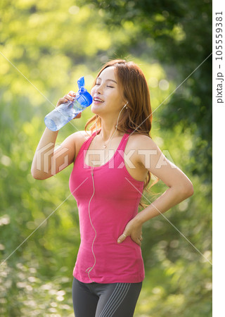 A beautiful woman holding a water bottle in the park while listening to music during morning exercise 105559381