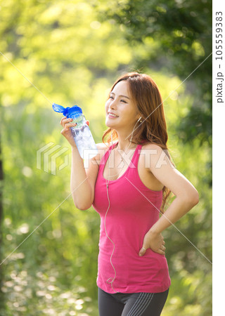 A beautiful woman holding a water bottle in the park while listening to music during morning exercise 105559383