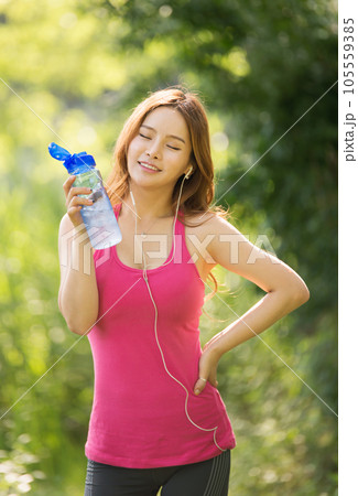 A beautiful woman holding a water bottle in the park while listening to music during morning exercise A beautiful woman holding a water bottle in the park while listening to music during morning exercise 105559385
