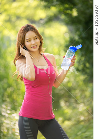 A beautiful woman holding a water bottle in the park while listening to music during morning exercise A beautiful woman holding a water bottle in the park while listening to music during morning exercise 105559397