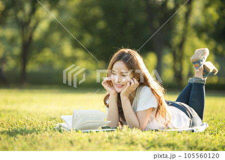 a beautiful woman lying on the park lawn reading 105560120
