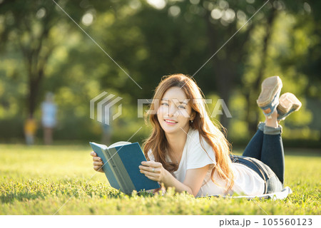 a beautiful woman lying on the park lawn reading 105560123
