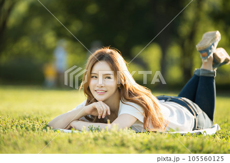 a beautiful woman lying on the park lawn reading 105560125