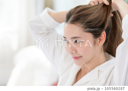 Beautiful Asian young woman tie the hair back before shower or apply cream or lotion on face. Beauty female grab her hairs after wake up with happiness and positive emotional. Self care concept 105560287