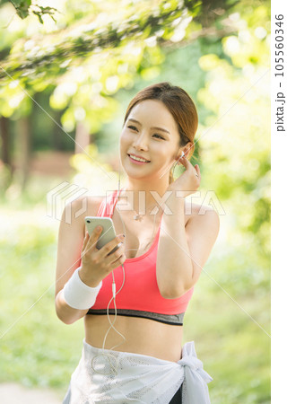 A beautiful woman wearing sportswear and exercising while listening to music on her smartphone in the park 105560346
