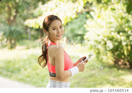 A beautiful woman wearing sportswear and exercising while listening to music on her smartphone in the park A beautiful woman wearing sportswear and exercising while listening to music on her smartphone in the park 105560514
