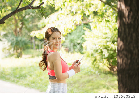 A beautiful woman wearing sportswear and exercising while listening to music on her smartphone in the park A beautiful woman wearing sportswear and exercising while listening to music on her smartphone in the park 105560515