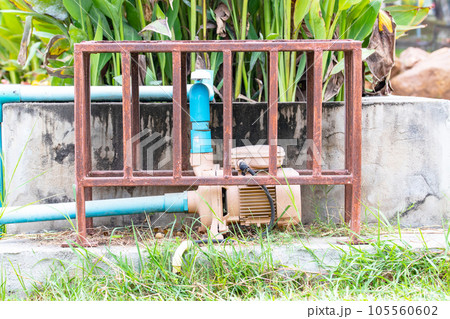Small water pump and motor broken damaged old rusty pipes. Installed next to pond in the park. There is plastic water pipe to pump water. surrounded by weeds that. Electric leakage safety concept. Small water pump and motor broken damaged old rusty pipes. Installed next to pond in the park. There is plastic water pipe to pump water. surrounded by weeds that. Electric leakage safety concept. 105560602
