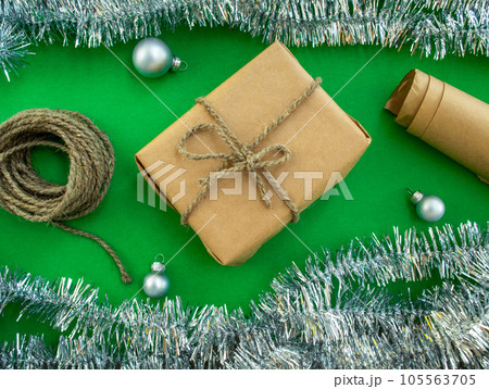 Christmas gift wrapping. A gift in craft paper, twine, paper, tinsel and Christmas balls on a green background. 105563705