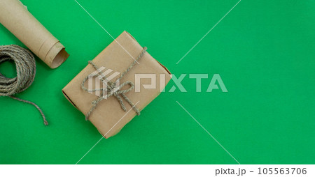 Christmas gift wrapping. Gift in craft paper, twine, paper on a green background. Christmas gift wrapping. Gift in craft paper, twine, paper on a green background. 105563706