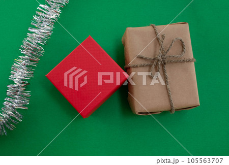 New Year gifts. A gift in craft paper, a gift in a red box and tinsel on a green background. 105563707