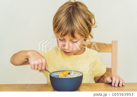 Happy boy sitting and eating a fresh smoothie bowl with mango, dragon fruit, granola and chia seeds Happy boy sitting and eating a fresh smoothie bowl with mango, dragon fruit, granola and chia seeds 105563953