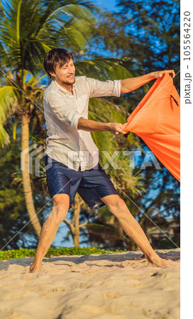 Summer lifestyle portrait of man inflates an inflatable orange sofa on the beach of tropical island. Relaxing and enjoying life on air bed VERTICAL FORMAT for Instagram mobile story or stories size 105564220