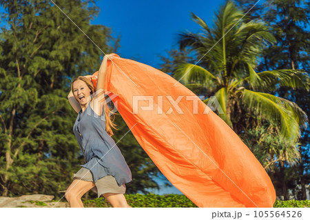 Summer lifestyle portrait of woman inflates an inflatable orange sofa on the beach of tropical island. Relaxing and enjoying life on air bed 105564526
