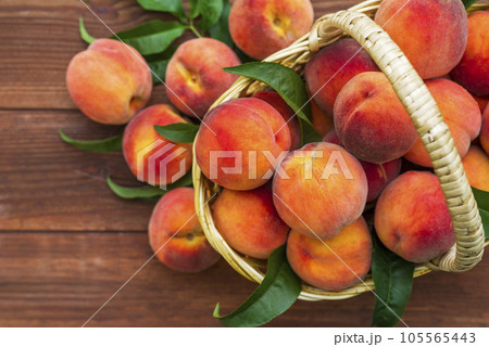 Fresh juicy peaches with leaves in a wicker basket on a wooden background.  105565443