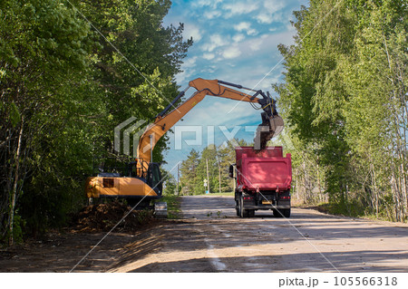 Crawler excavator pours dirt into dump truck during roadworks on country road. 105566318