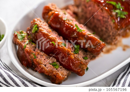 Slicing classic meatloaf with a sweet glaze on a white serving plate Slicing classic meatloaf with a sweet glaze on a white serving plate 105567196