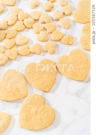 Decorating heart-shaped sugar cookies with pink and white royal icing for Valentine's Day. Decorating heart-shaped sugar cookies with pink and white royal icing for Valentine's Day. 105567526